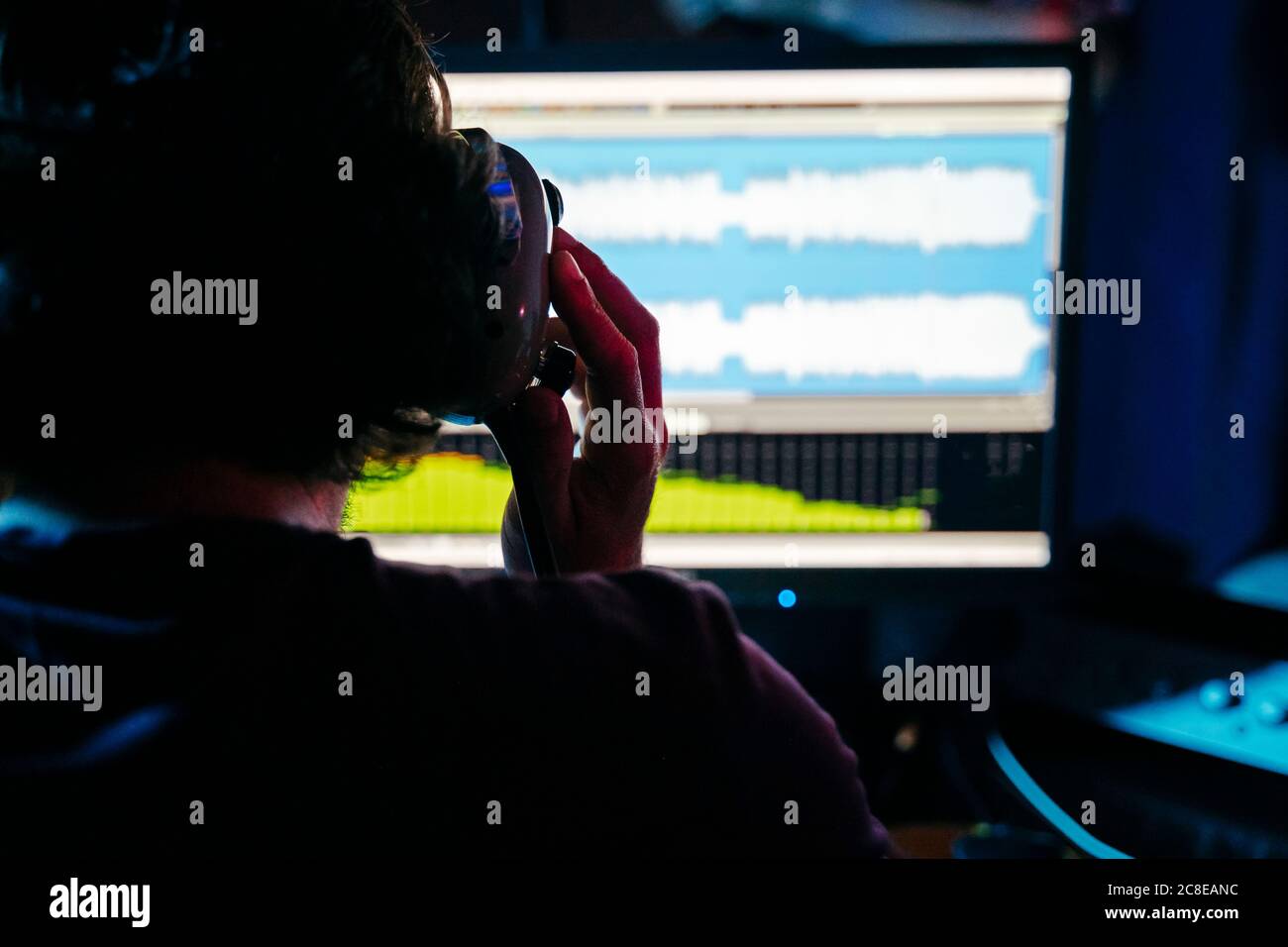 Uomo che tiene le cuffie mentre usa il computer in studio di registrazione a. casa Foto Stock