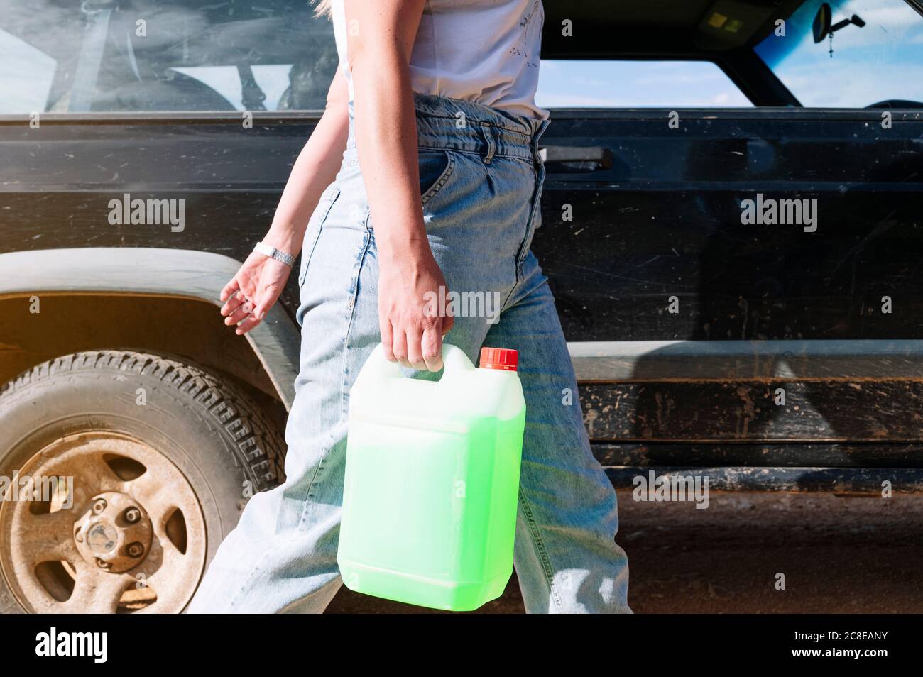 Sezione centrale della donna che trasporta il contenitore del gallone di refrigerante mentre cammina veicolo 4x4 in giornata di sole Foto Stock