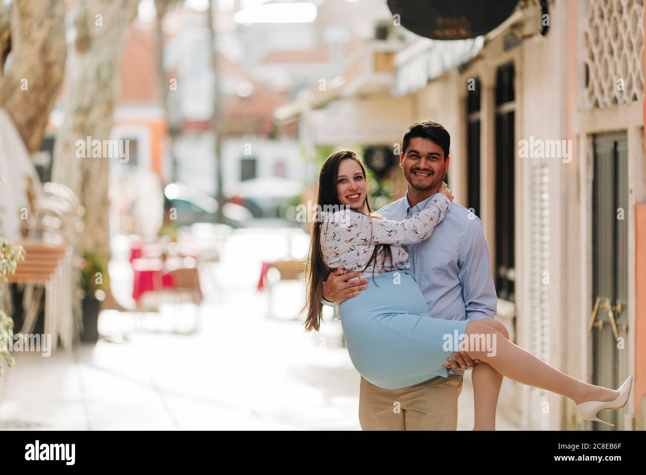 Uomo felice che porta una donna incinta in città durante il giorno di sole Foto Stock