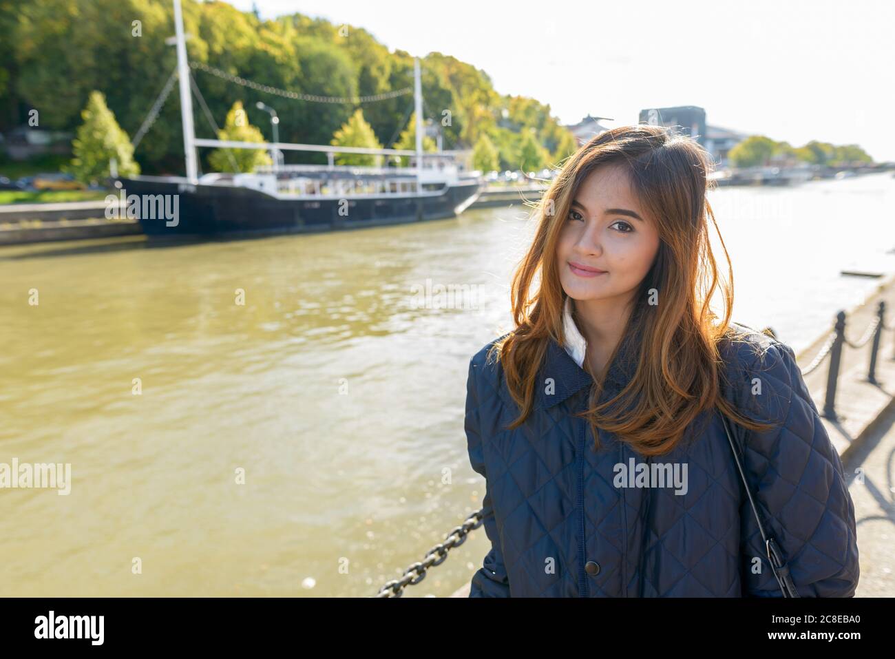 Giovane bella donna asiatica in piedi nel molo con vintage barca nera nel fiume Foto Stock