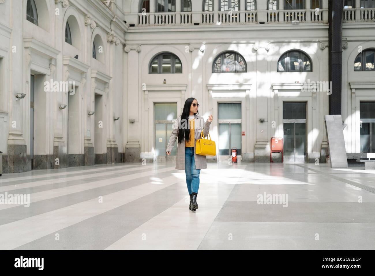 Giovane donna elegante che cammina sul pavimento contro l'edificio Foto Stock