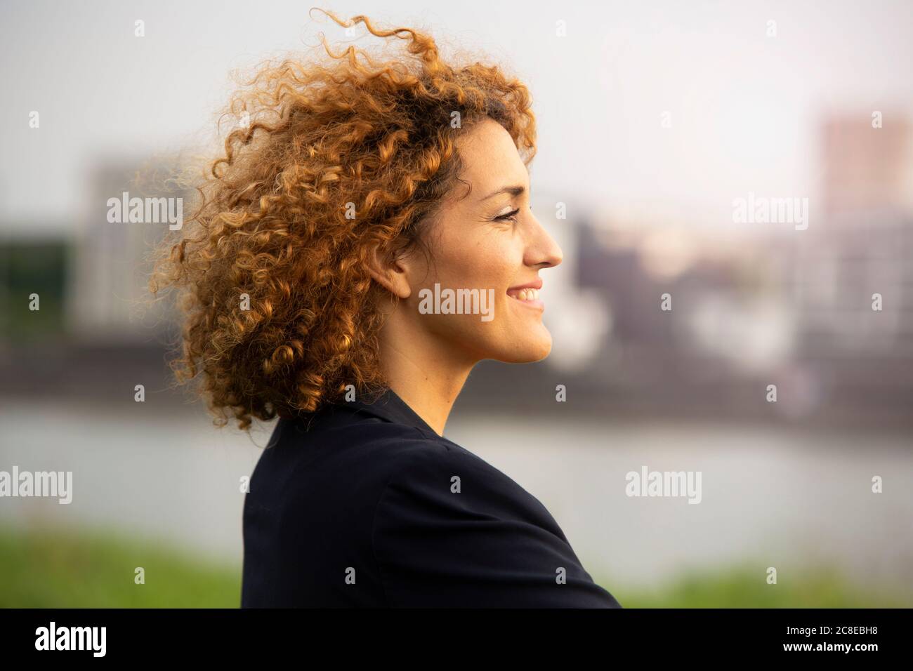 Primo piano di una donna d'affari sorridente con capelli ricci che guarda via dentro città Foto Stock