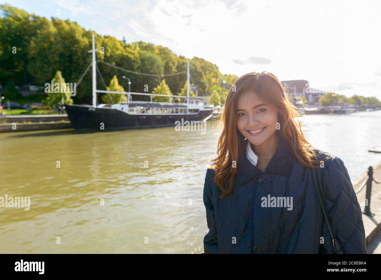 Giovane donna asiatica felice in piedi nel molo con vintage barca nera nel fiume Foto Stock
