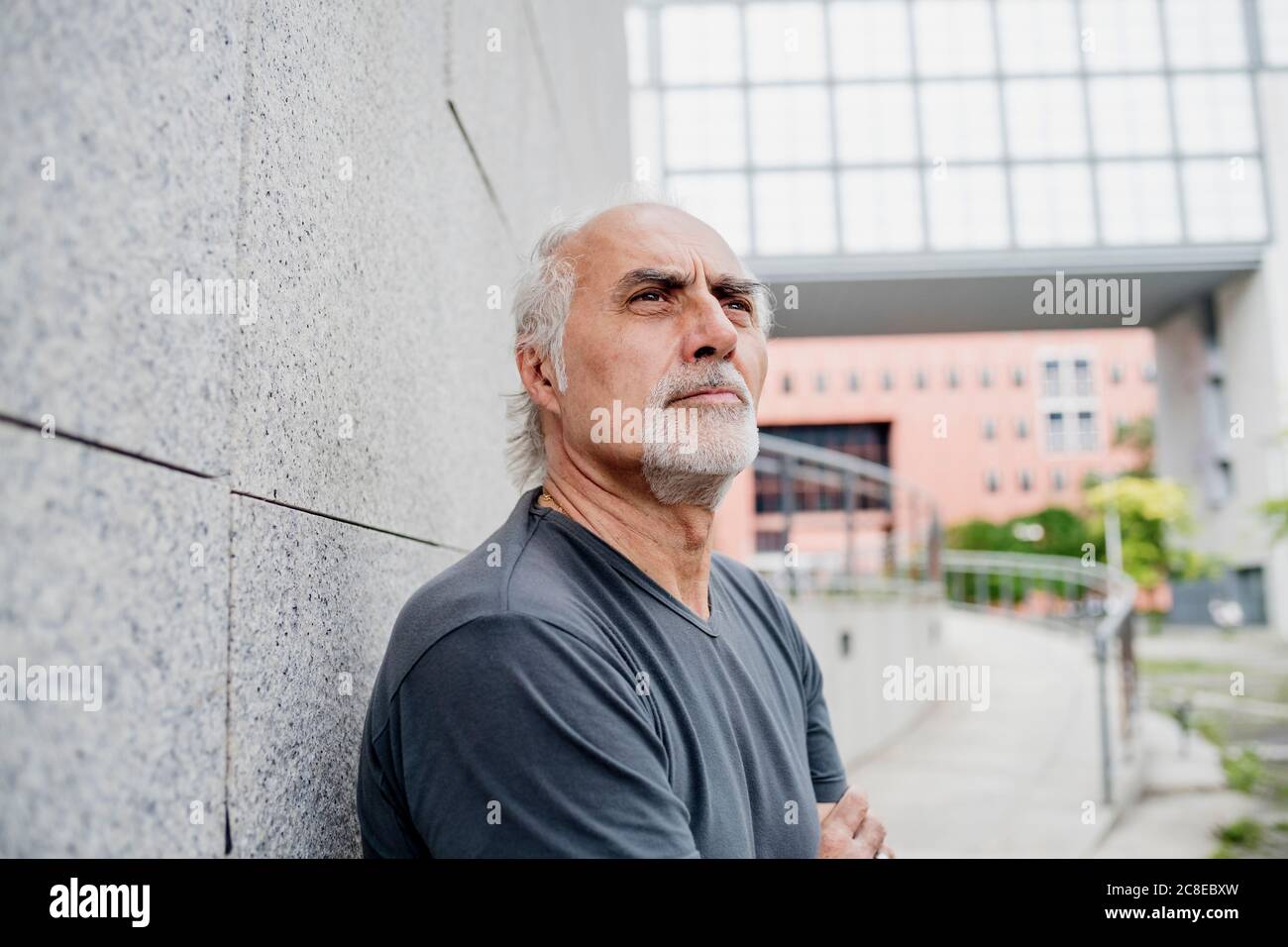 Primo piano di un uomo senior attento che guarda lontano mentre si sta in piedi parete Foto Stock