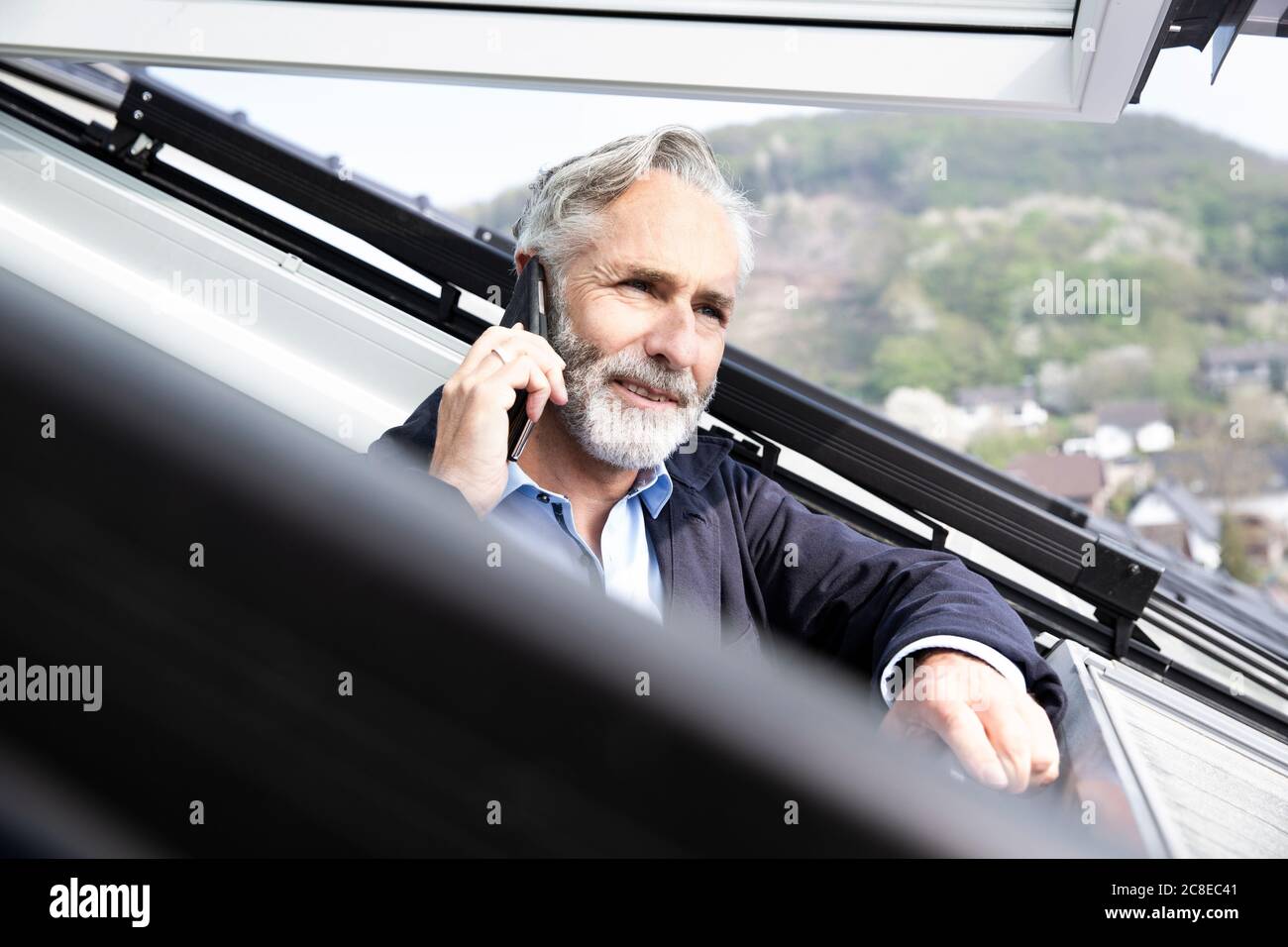 Primo piano di un architetto maschile che parla di smartphone in casa vista attraverso la finestra Foto Stock