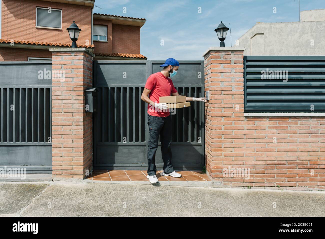 Lavoratore postale maschile utilizzando interfono mentre si sta con il pacchetto a. porta della casa Foto Stock