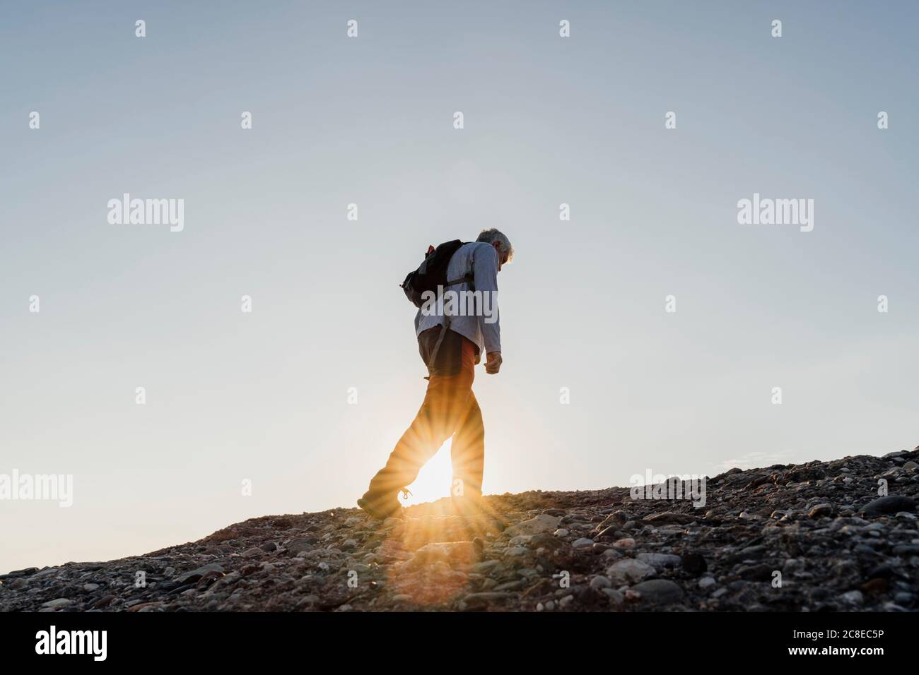 Sunbeam attraverso l'uomo anziano attivo escursioni in montagna contro il cielo Foto Stock