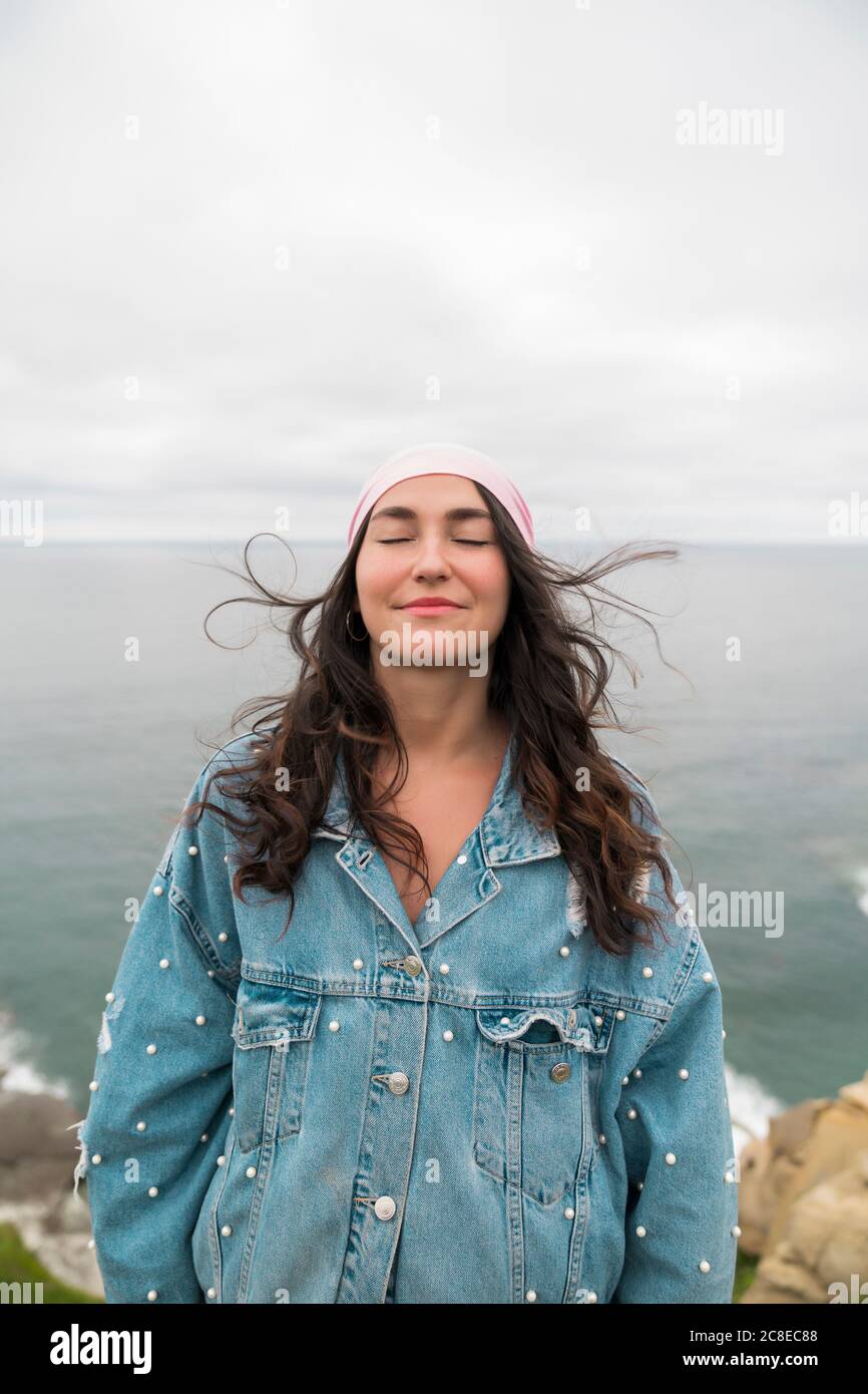 Sorridi donna sopravvissuta al cancro con occhi chiusi in piedi contro il mare Foto Stock