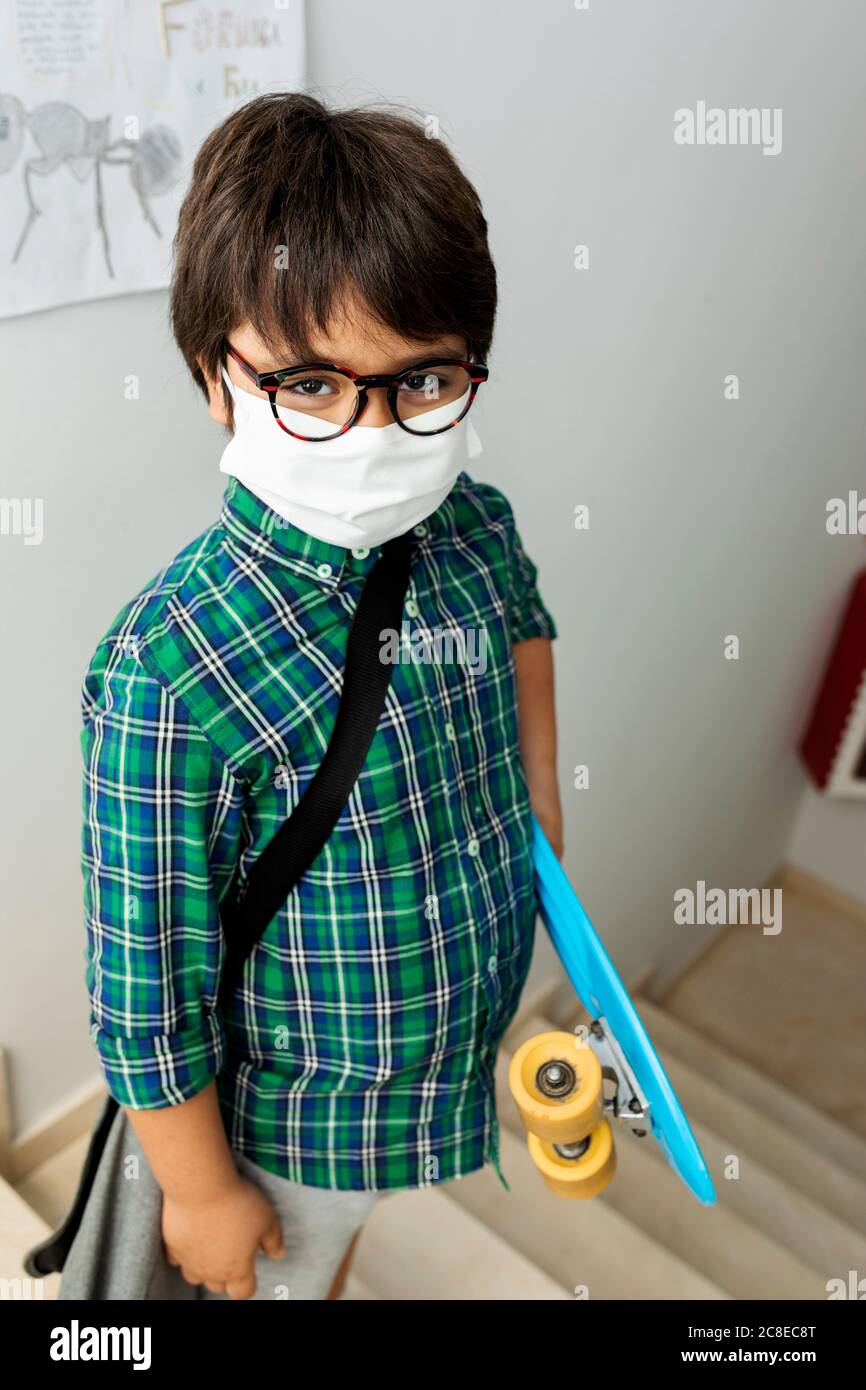 Ragazzo che indossa una maschera che tiene lo skateboard mentre si trova sui gradini scuola Foto Stock