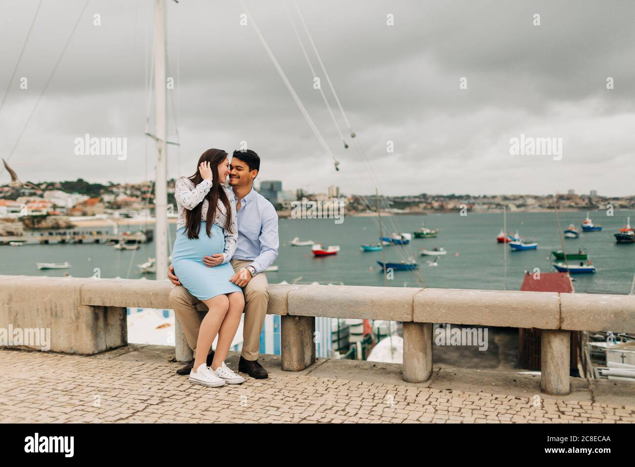 Una romantica coppia in attesa che siede su un muro di contenimento al porto di Cascais, Portogallo Foto Stock