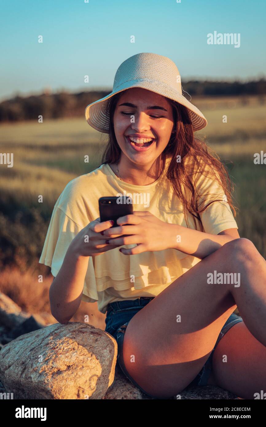 Giovane donna allegra che usa lo smartphone sul campo durante il tramonto Foto Stock