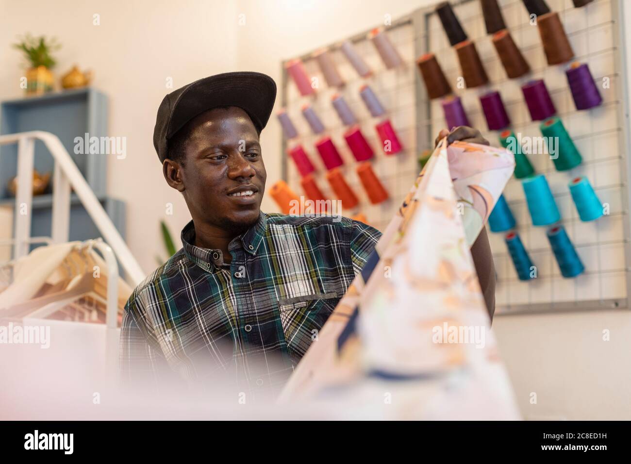 Sorridente giovane fashion disegnando tirocinante guardando il tessuto in atelier Foto Stock
