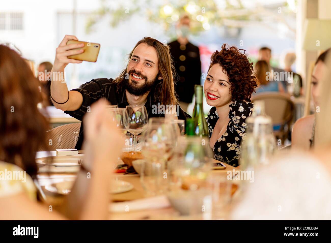 Sorridente giovane uomo bearded che prende selfie con la donna seduta a. tavolo nel ristorante Foto Stock