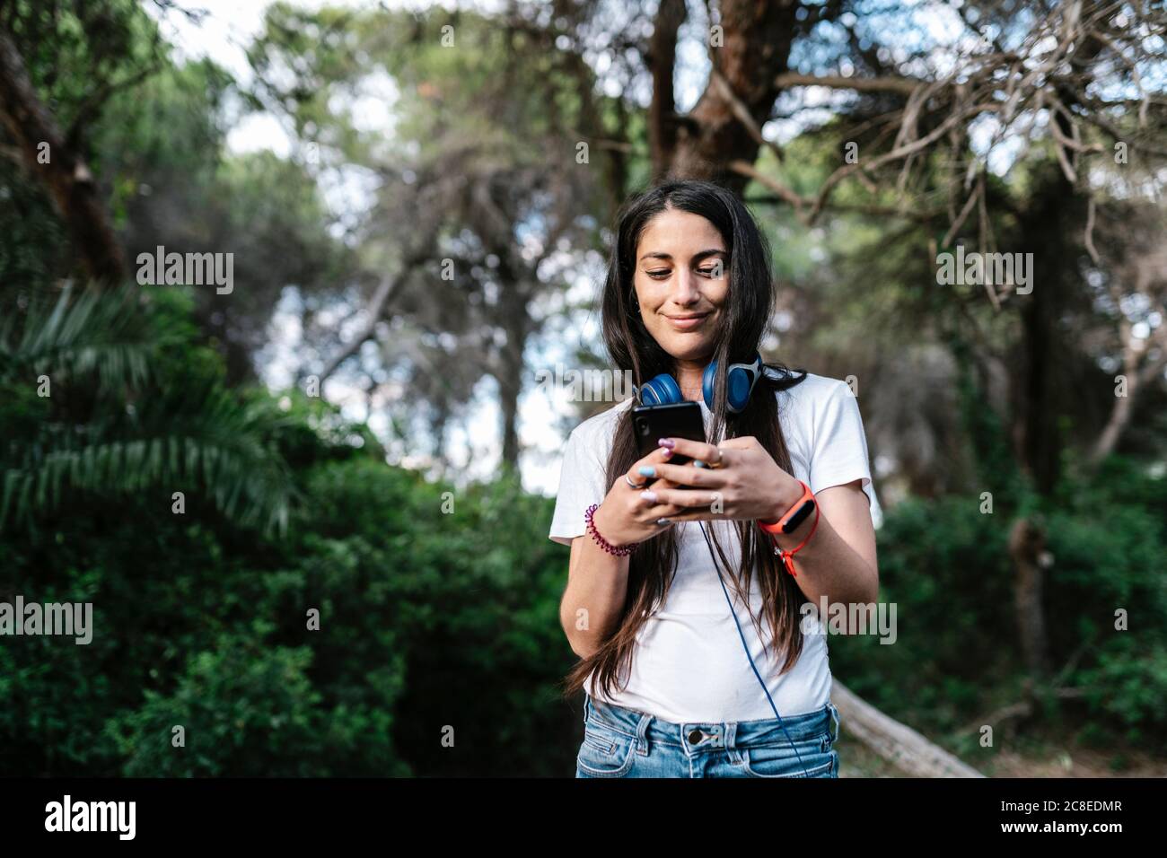Donna con auricolare che utilizza lo smartphone nel bosco Foto Stock