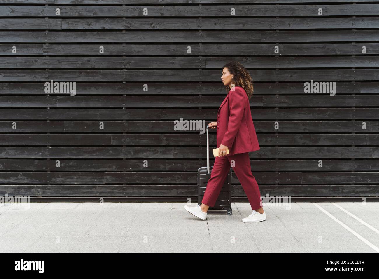 Giovane donna professionista a piedi con bagagli sul sentiero di nero muro di legno in città Foto Stock