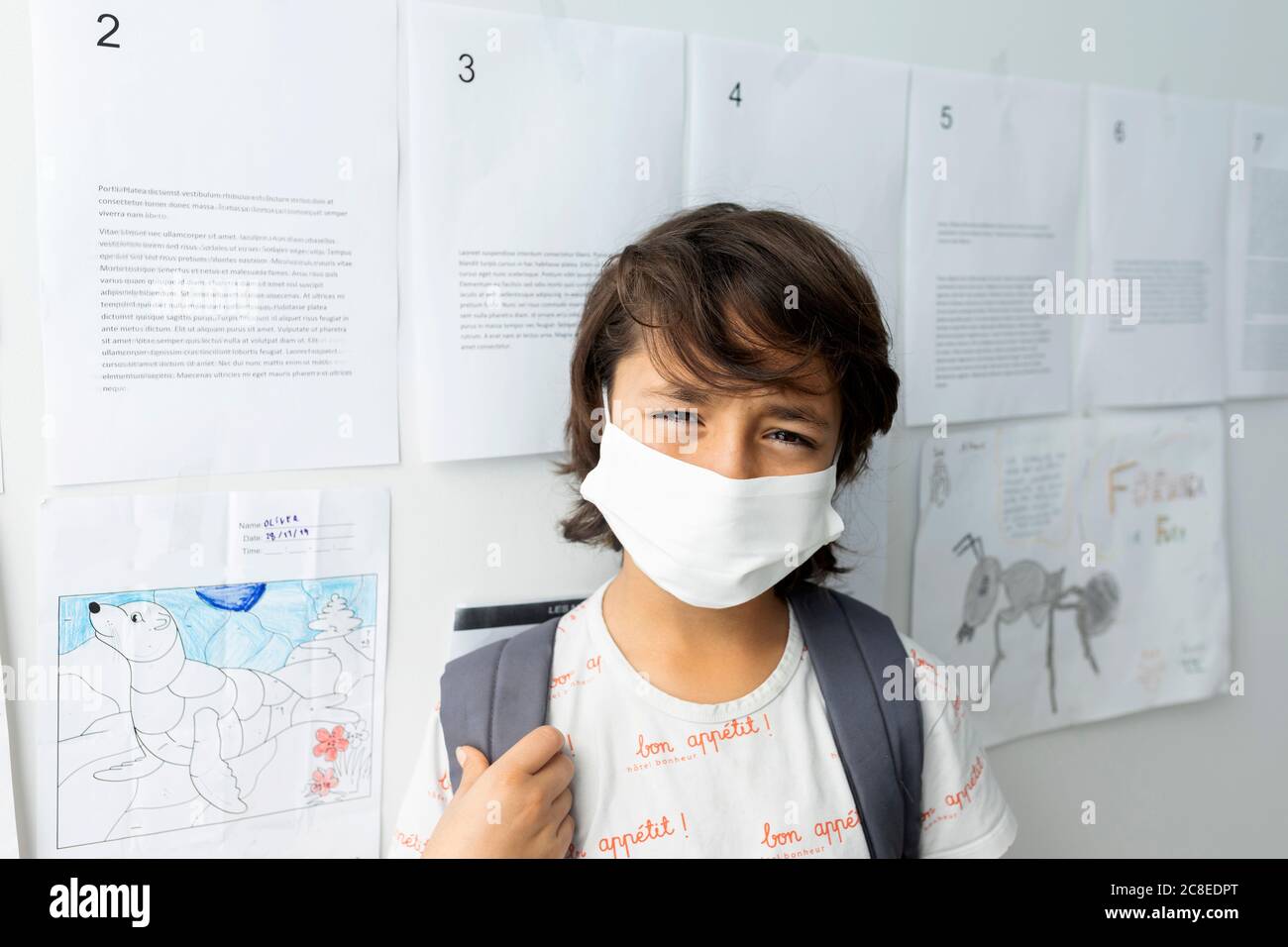 Primo piano di ragazzo che indossa una maschera in piedi contro carte attaccate muro a scuola Foto Stock