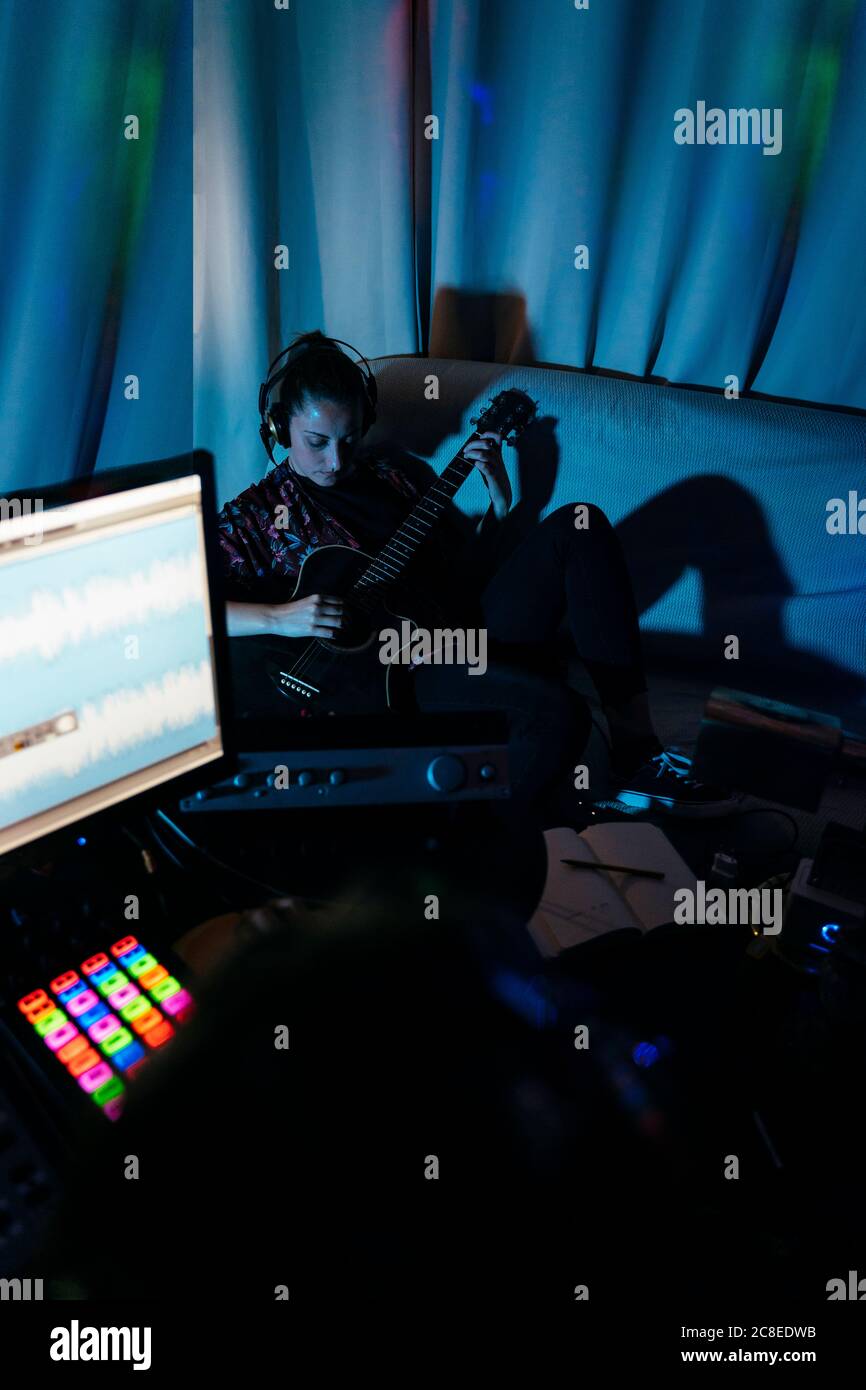 Donna che suona la chitarra mentre l'uomo usa il computer in studio di registrazione a casa Foto Stock