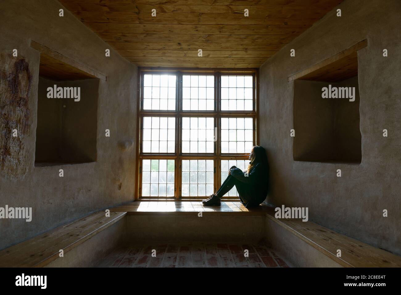 Giovane donna seduta di fronte a una finestra di legno chiusa con luce solare che si difudeva Foto Stock