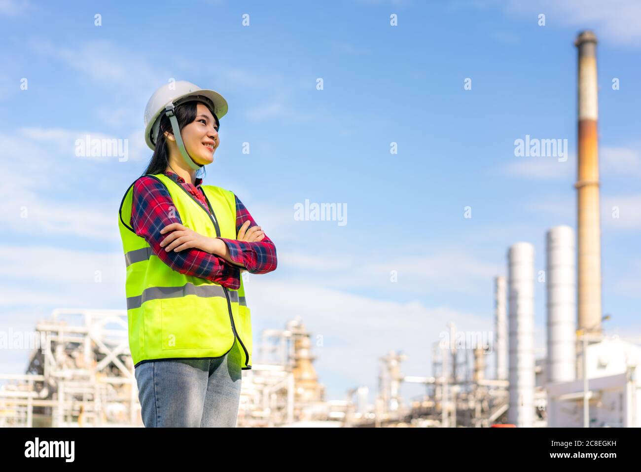 Donna asiatica ingegnere braccio attraversato e sorriso con fiducioso in attesa di futuro con la fabbrica di raffineria di petrolio in background. Foto Stock
