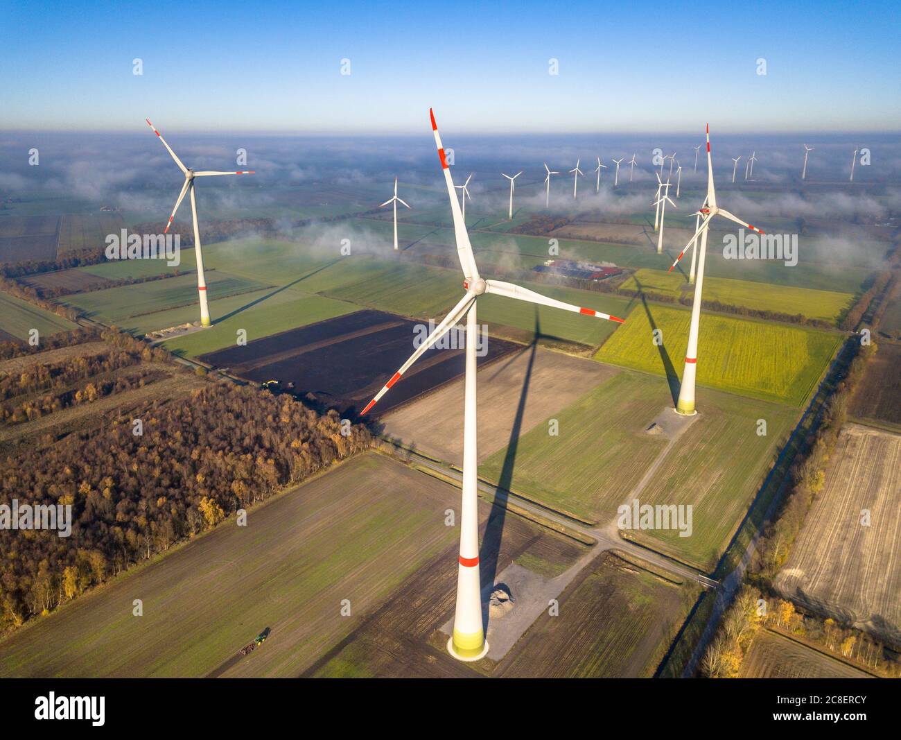 Vista aerea dell'energia eolica turbine di centrali eoliche sopra lo strato di nebbia sulla campagna tedesca al sole del mattino. Germania Foto Stock