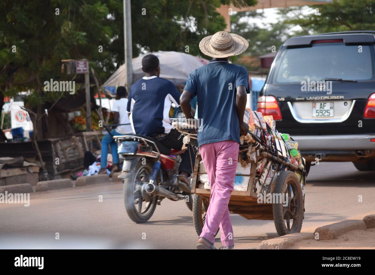 Un venditore in viaggio che spinge il suo carrello caricato con gli articoli giù una strada occupata a Niamey, Niger, Africa Foto Stock