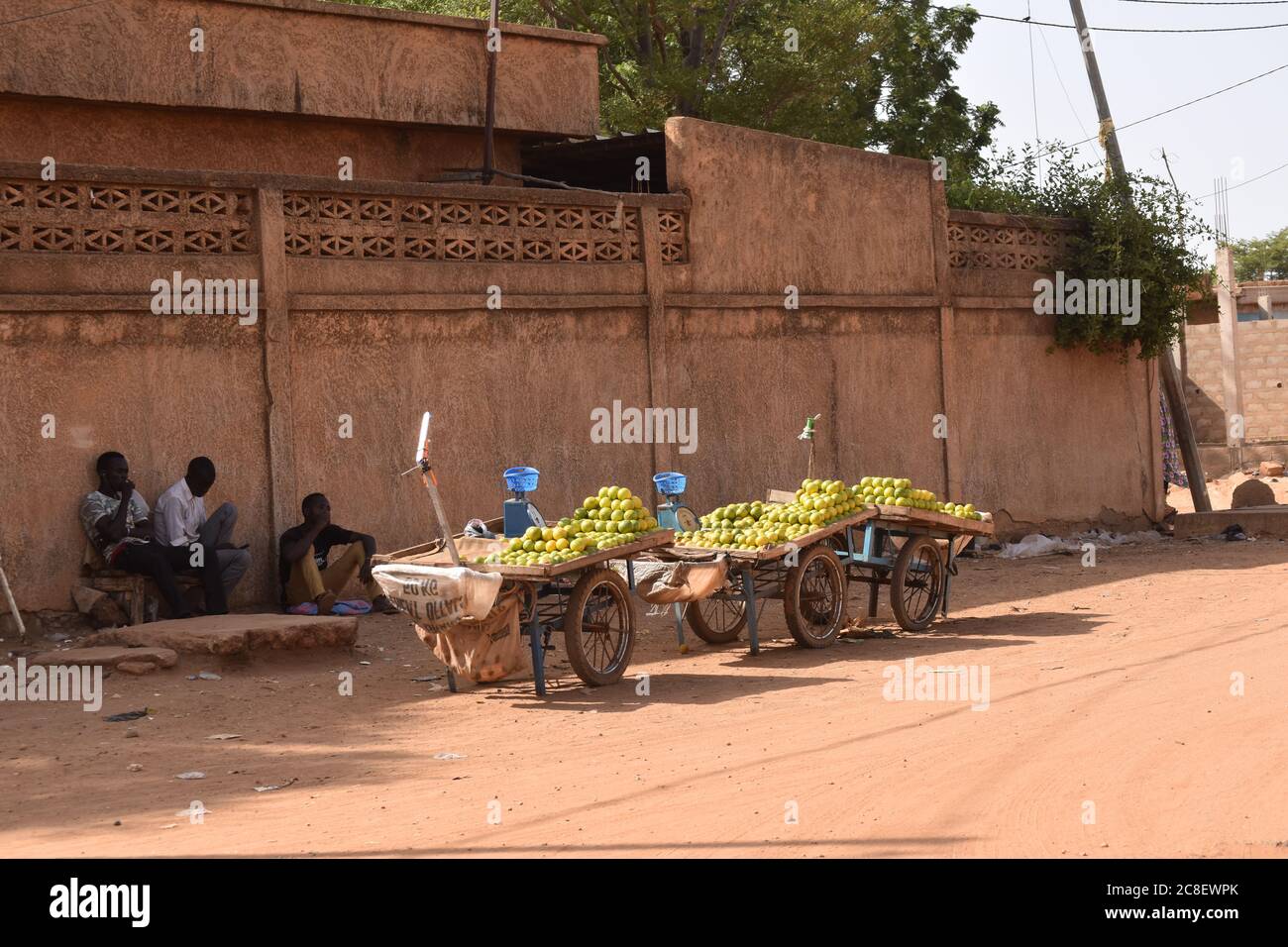 Tre carrelli di spinta caricati con arance per la vendita siedono sul lato di una strada mentre i loro proprietari riposano all'ombra, a Niamey, Niger, Africa. Foto Stock