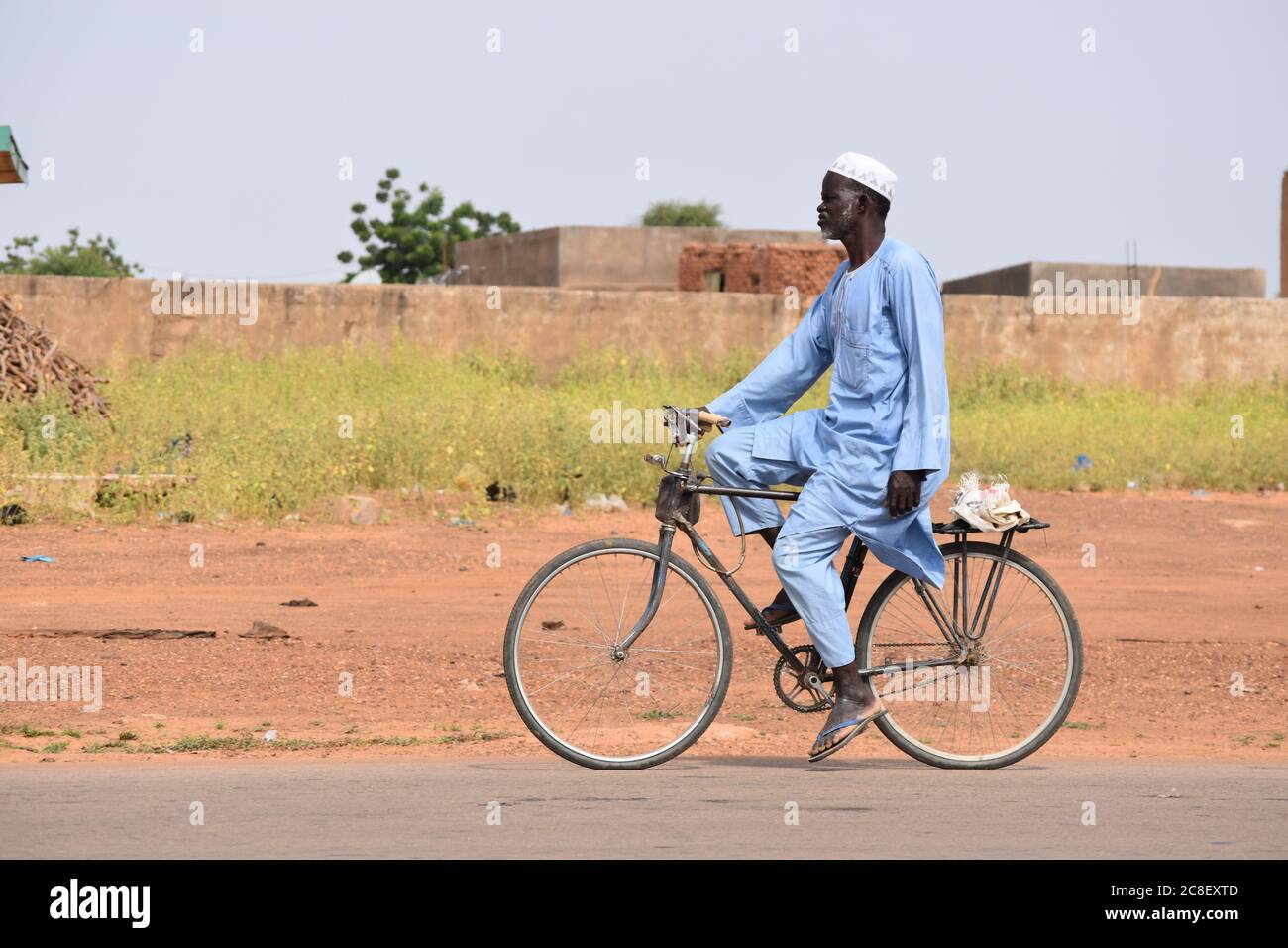 Un uomo anziano che guida una pedalata attraverso un villaggio africano. Foto Stock