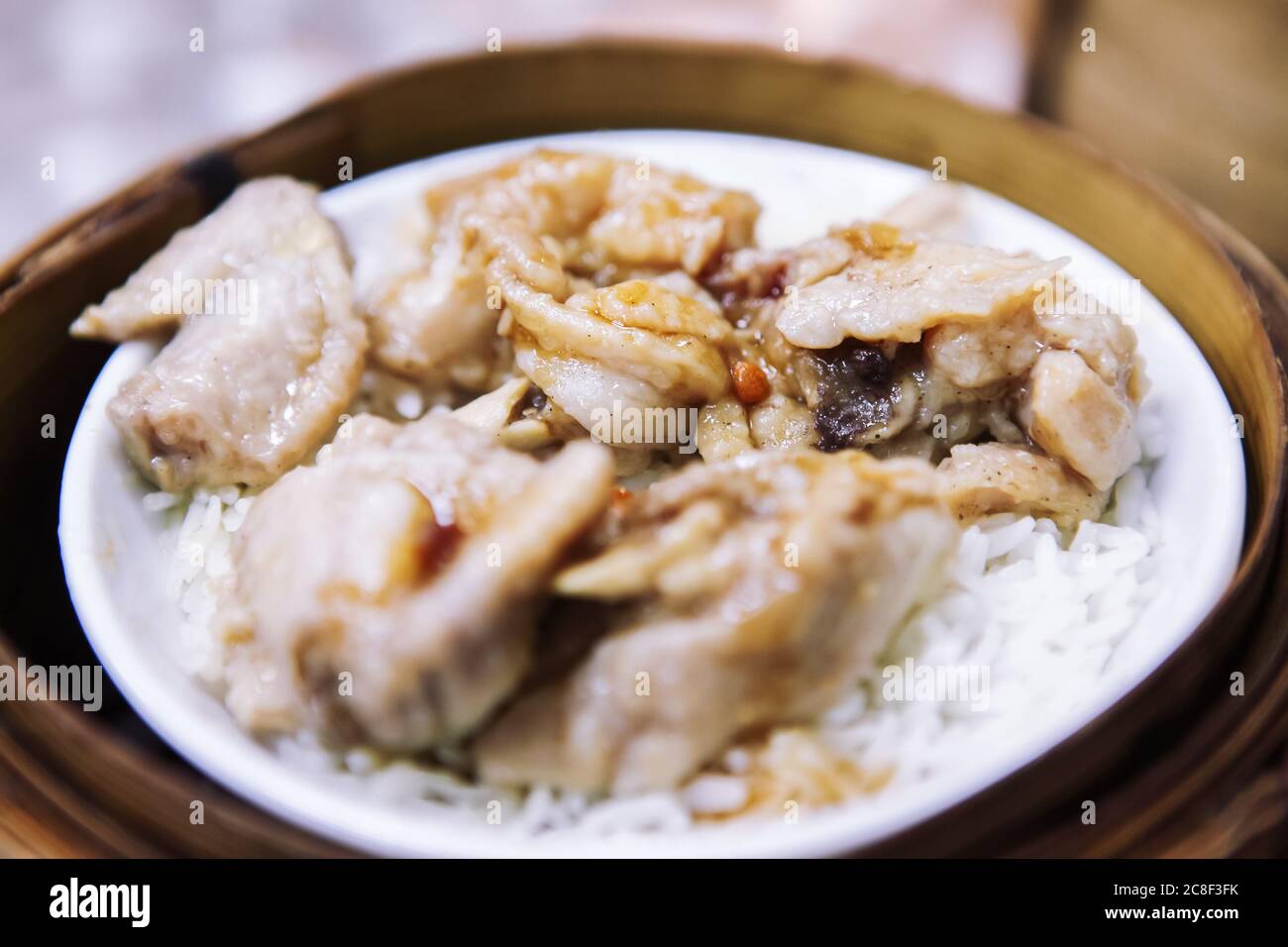 Cuocere il pollo con riso bianco in un recipiente bianco con un cesto di vapore di bambù come base. Foto Stock