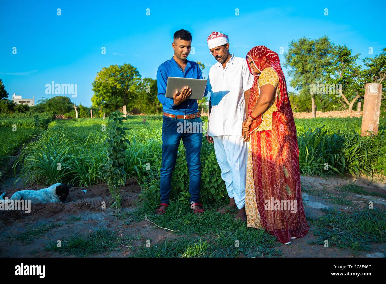 Giovane indiano con computer portatile che mostra qualcosa per la famiglia contadina villaggio su internet in piedi in campo verde, terra agricola, computer di insegnamento e u Foto Stock