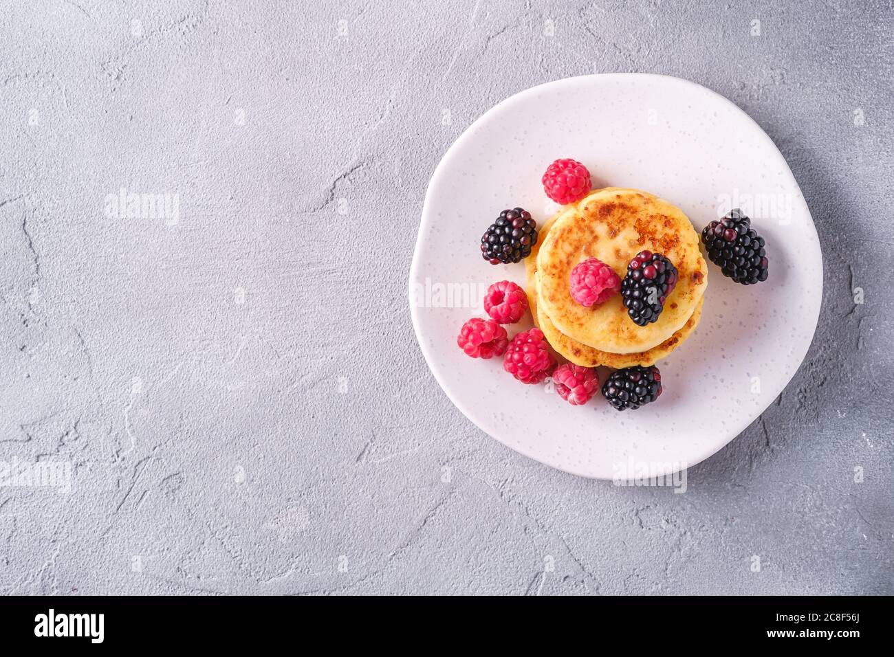 Frittelle al formaggio, frittelle di cagliata dessert con lampone e frutti di mora in piastra su fondo di pietra in cemento, spazio copia vista dall'alto Foto Stock