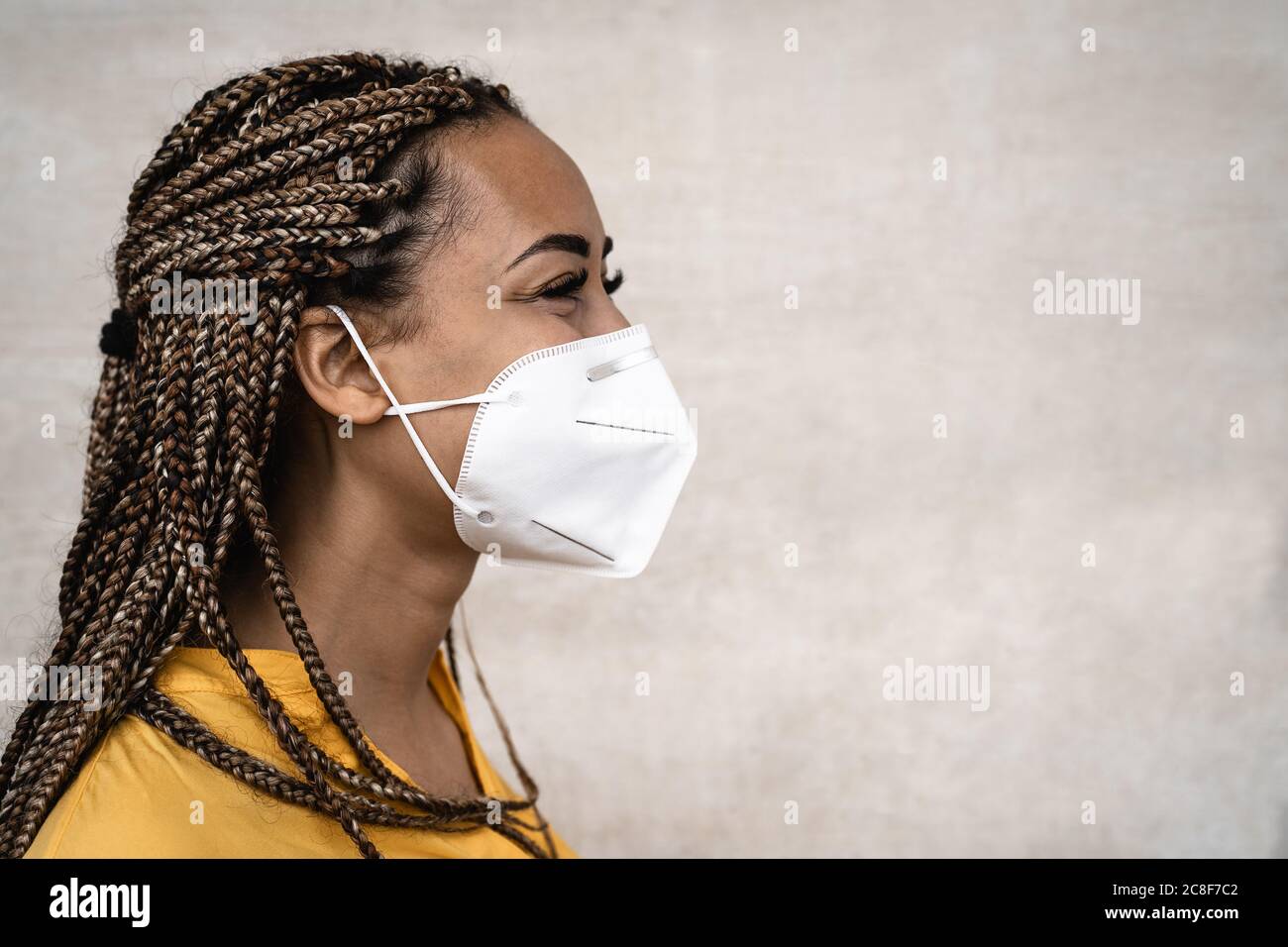 Donna africana con trecce che indossano maschera medica facciale - giovane ragazza che usa il facemask per prevenire e fermare la diffusione del virus corona Foto Stock