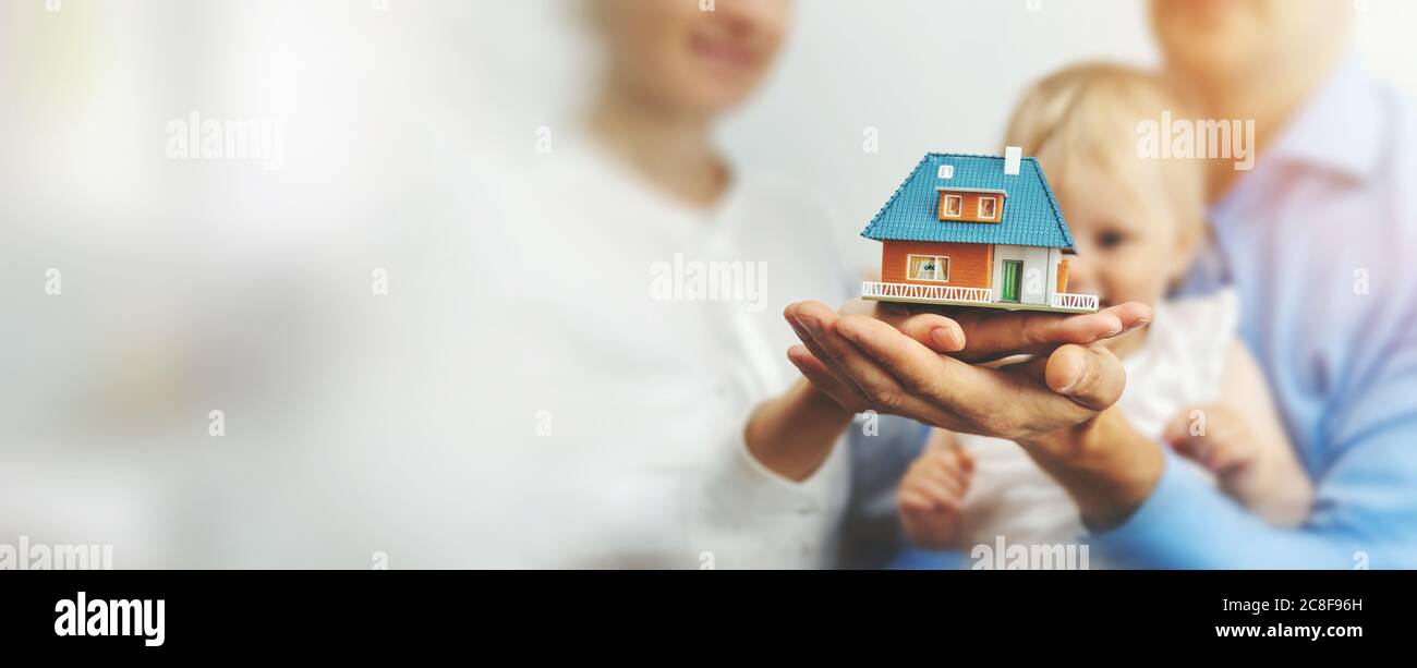 nuovo concetto di casa di famiglia - i genitori giovani e il bambino con modello di scala della casa di sogno nelle mani. spazio di copia Foto Stock