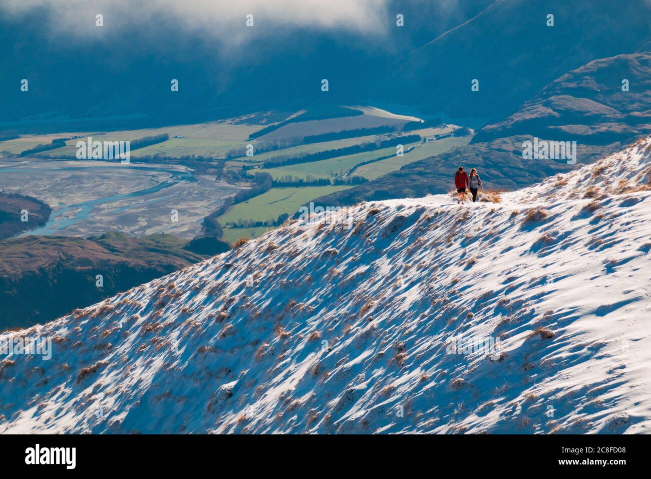 Due turisti camminano su una pista innevata fino a Roys Peak, Wanaka, Nuova Zelanda Foto Stock