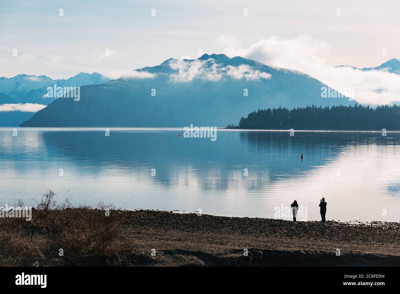 Un ragazzo e una ragazza scattano foto in una mattinata invernale perfettamente calma al Lago Wanaka, nell'Isola del Sud della Nuova Zelanda Foto Stock