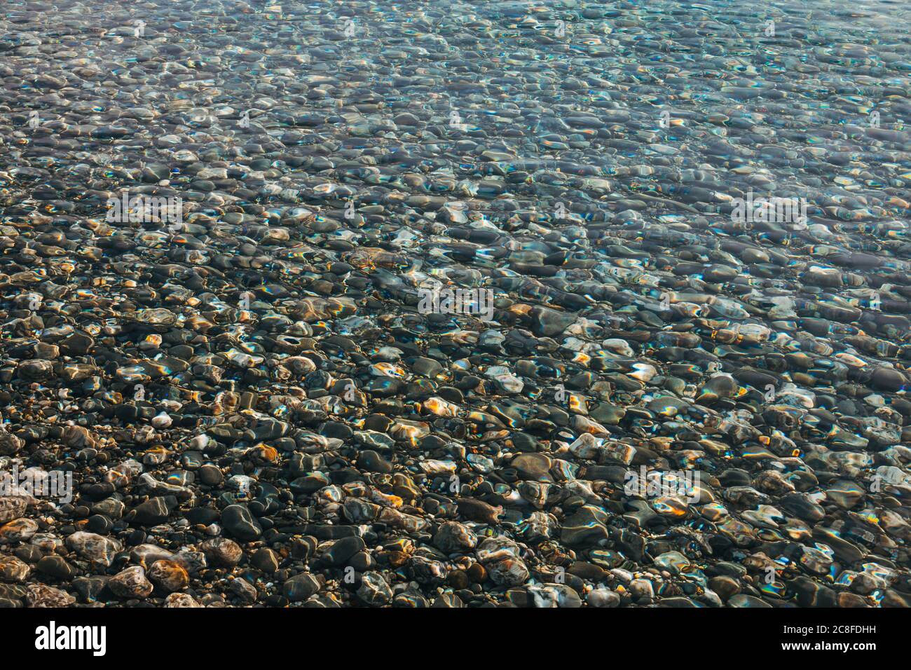 L'acqua cristallina rifrange la luce mentre si lava su ciottoli sulla riva e sul lago del lago Hawea, Nuova Zelanda Foto Stock