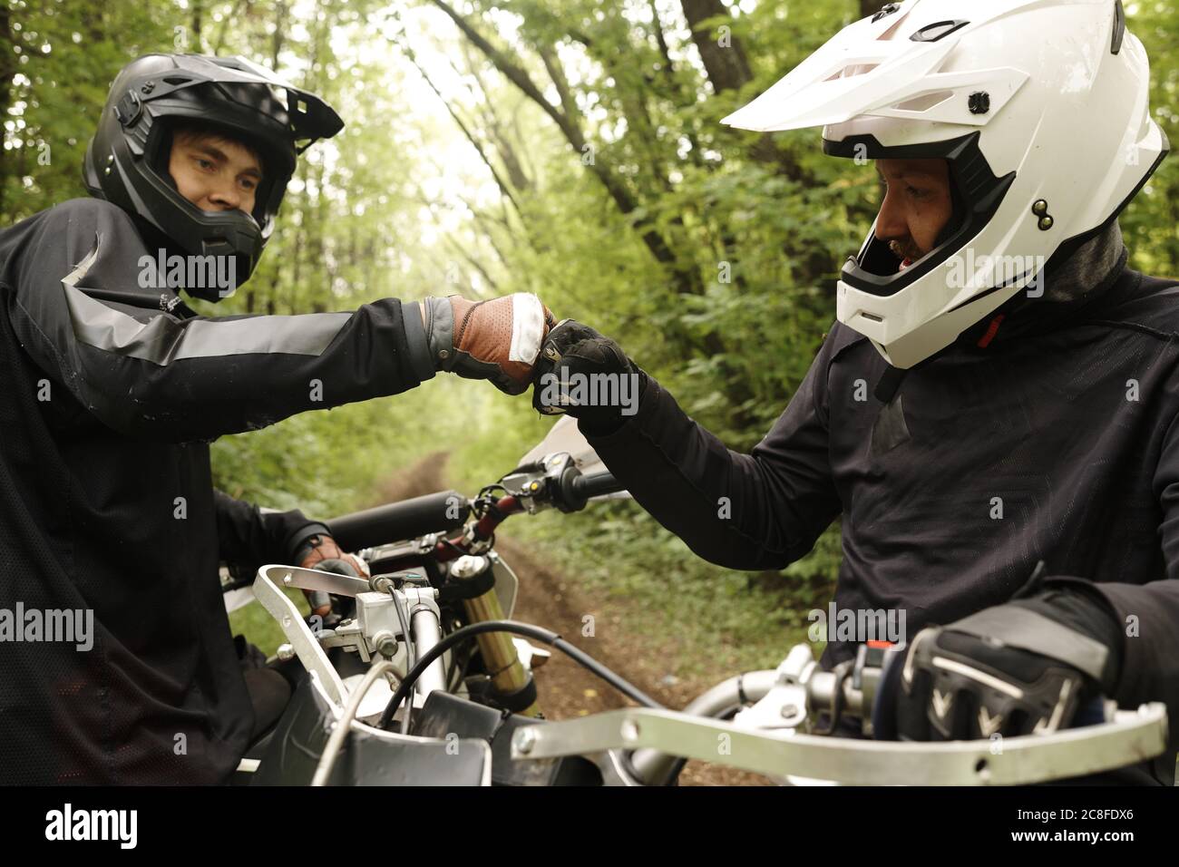 Amici maschi in caschi fare pugno pugno mentre si sostengono a vicenda, si godono il motociclismo in foresta Foto Stock