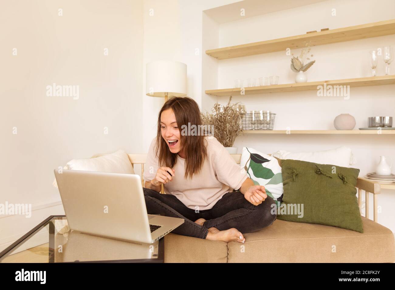 Donna sul divano a casa con un computer portatile che guarda la fotocamera Foto Stock