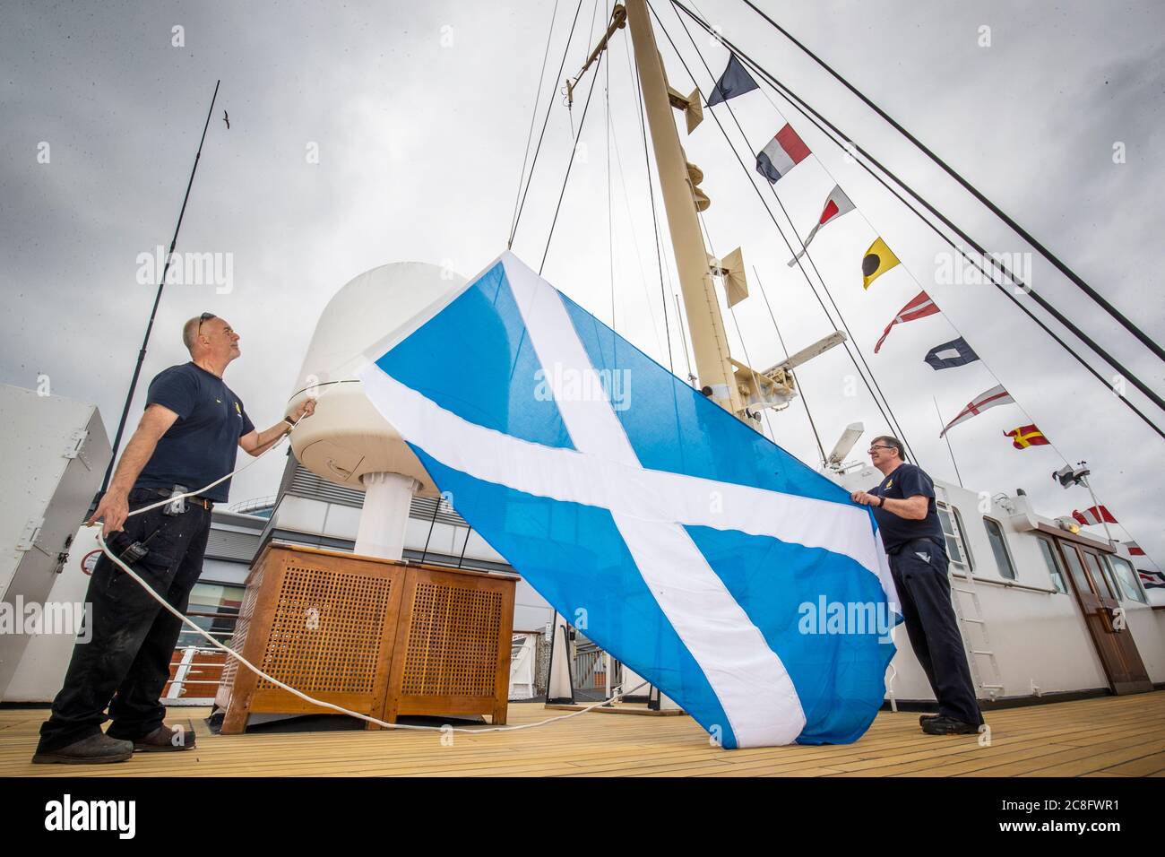 Rab McAulay (a sinistra) e Tony Smith, del team di manutenzione, alzano la bandiera del Sattyre sull'albero centrale del Royal Yacht Britannia per segnare la riapertura dell'attrazione turistica di Edimburgo ai membri del pubblico lunedì 27 luglio. Foto Stock