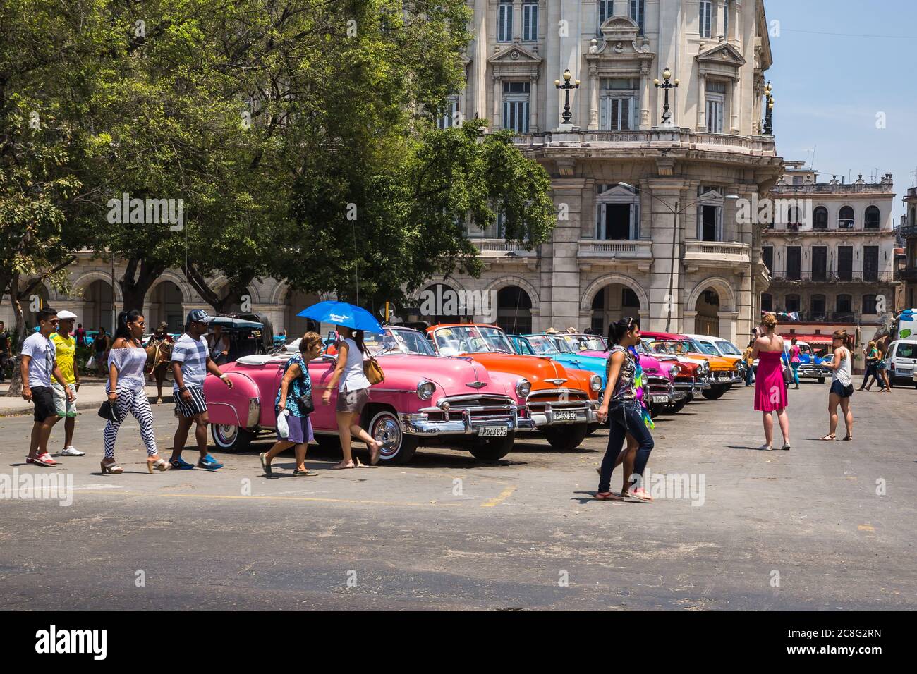 L'Avana / Cuba - 04.15.2015: Turisti e gente del posto camminano di fronte a colorate auto americane classiche che sono usate come taxi turistico a Cuba Foto Stock