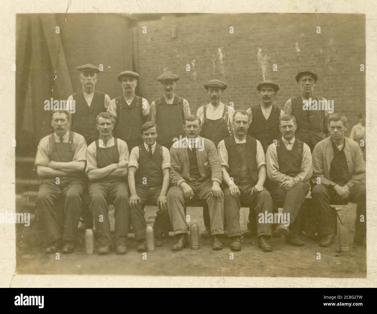 Cartolina degli inizi del 1900 di uomini in classe operaia all'esterno in cortile con tappi piatti, con matracci, circa 1907, Regno Unito Foto Stock