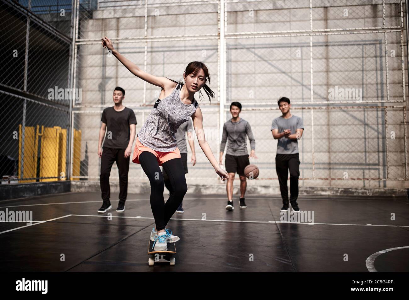 giovane donna asiatica skateboarder skateboarder all'aperto con amici che guardano da dietro Foto Stock