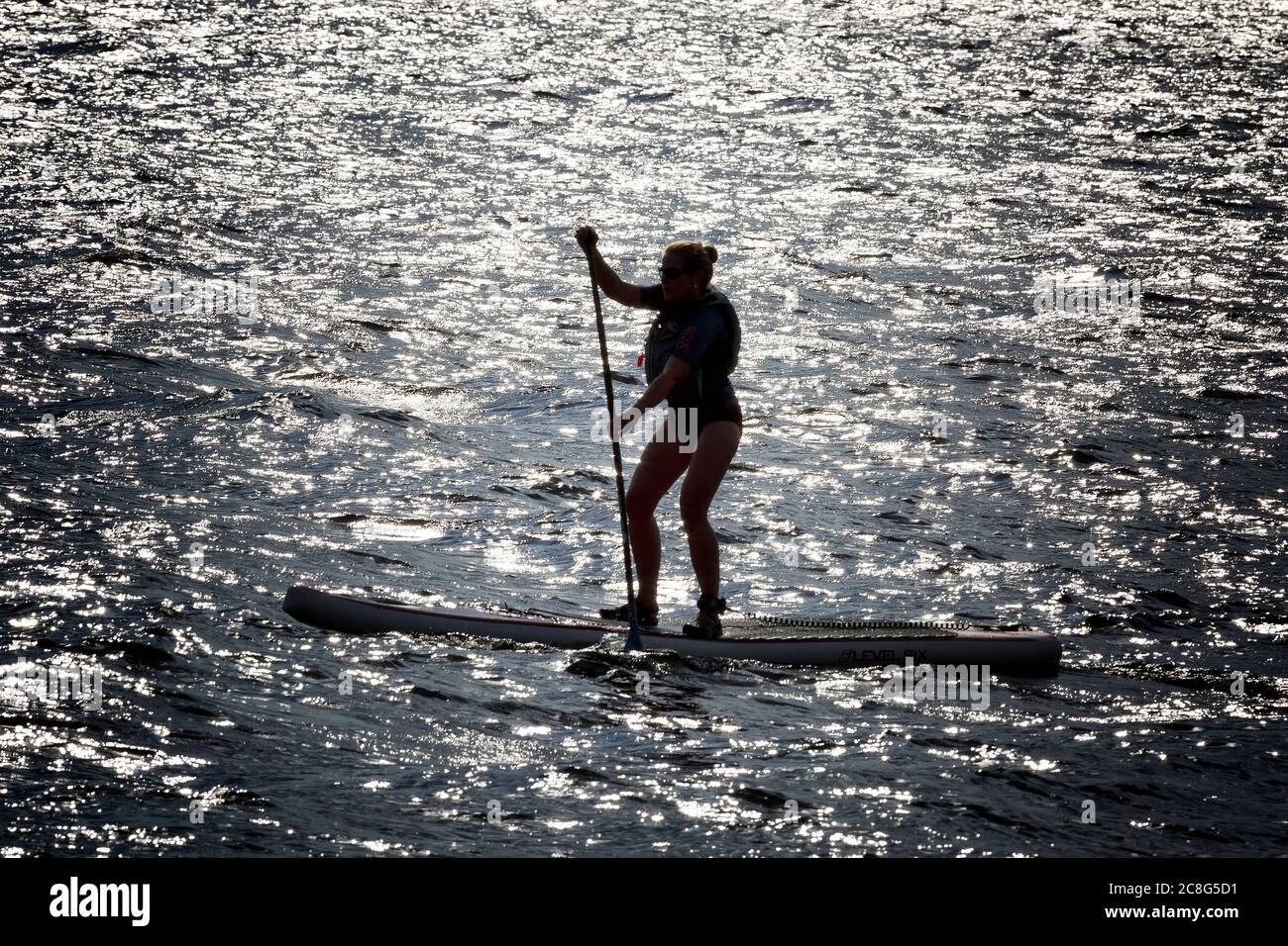 Giovane donna sul paddle board al tramonto. Foto Stock