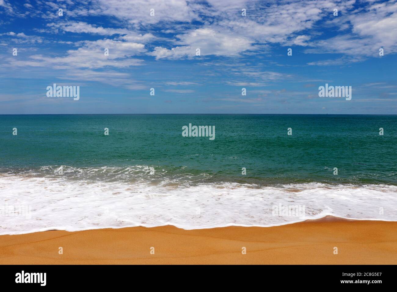Naviga su una spiaggia di sabbia tropicale, vista panoramica sulla costa vuota del mare con sabbia gialla e onde smeraldo con schiuma bianca. Pittoresco mare con cielo blu Foto Stock