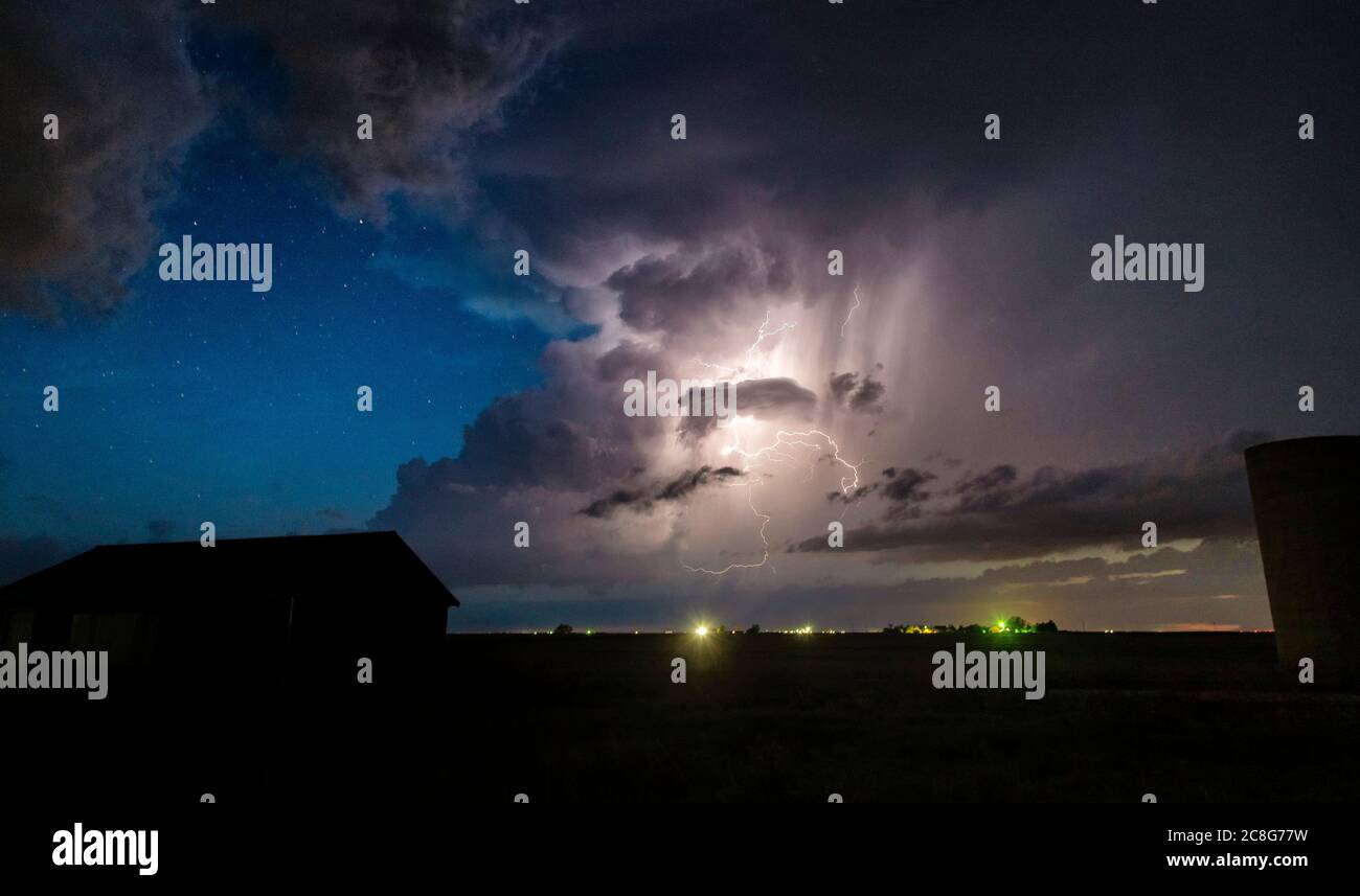 Numerosi fulmini da nuvola a nuvola si vedono lungo la linea secca di notte, con stelle sullo sfondo sopra gli edifici della fattoria Foto Stock