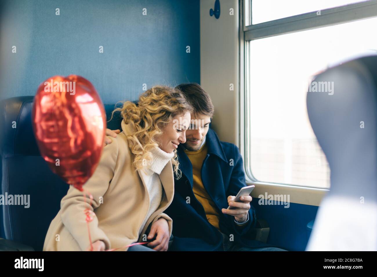 Coppia con cuore palloncino di forma utilizza lo smartphone all'interno del treno Foto Stock