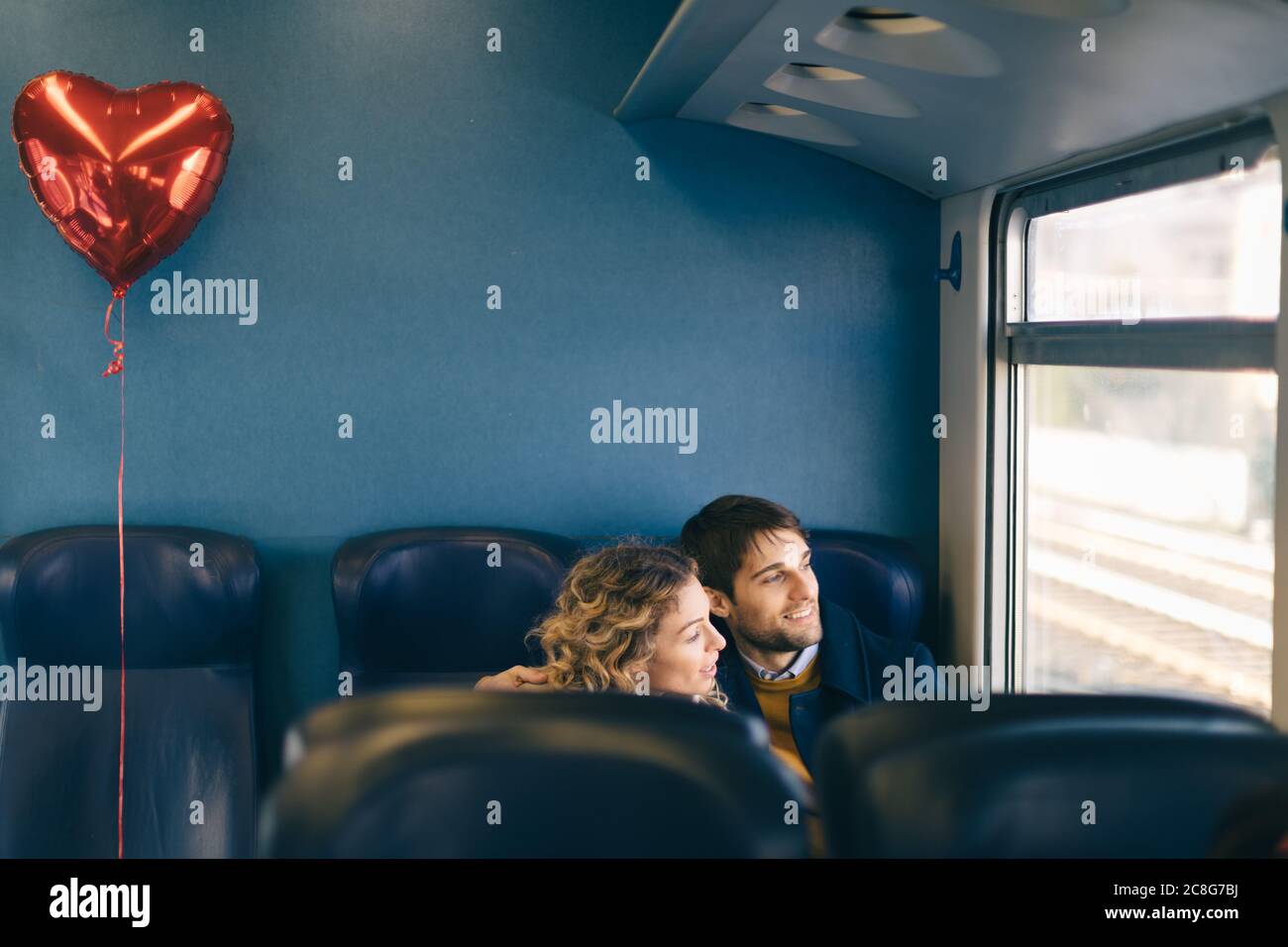 Coppia con cuore palloncino a forma di guardare fuori dalla finestra del treno Foto Stock