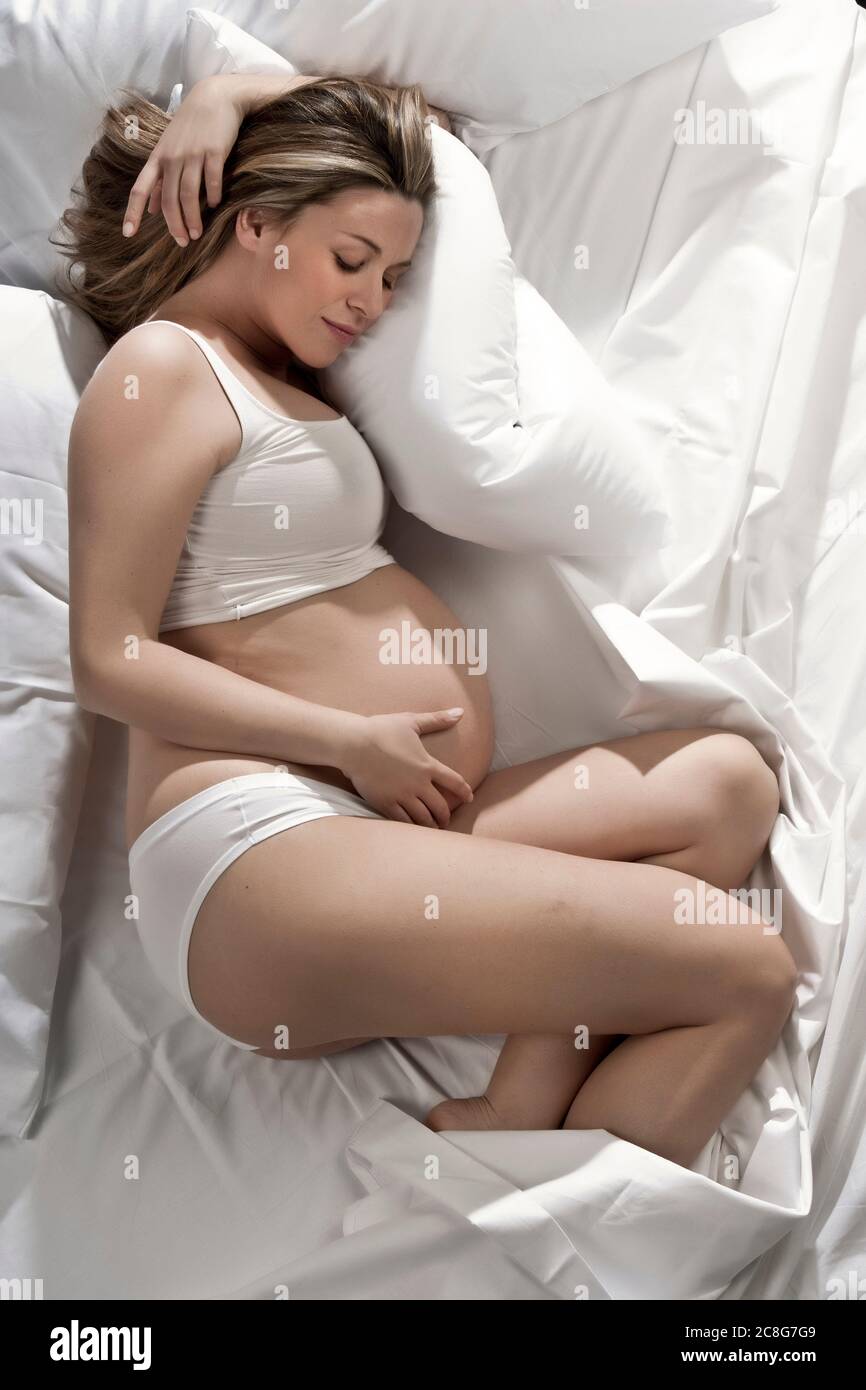 Ritratto di donna fortemente incinta sdraiata sul letto, culling stomaco. Foto Stock