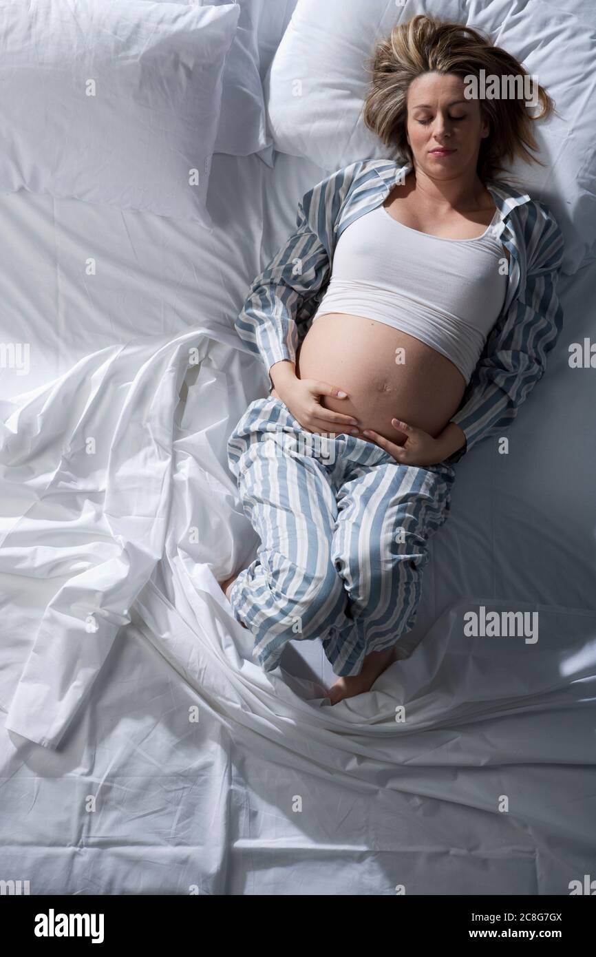 Ritratto di donna fortemente incinta sdraiata sul letto, culling stomaco. Foto Stock