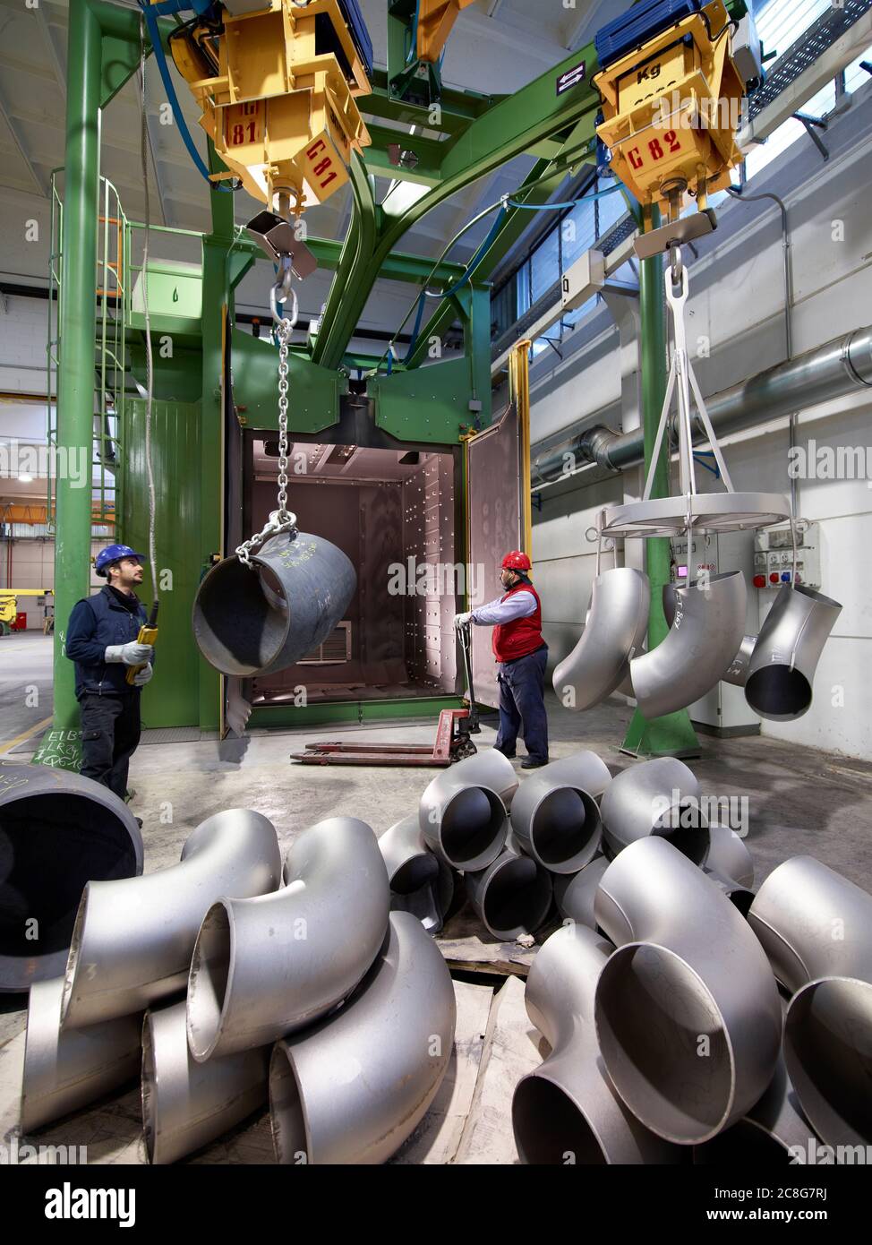 Uomini che lavorano in una fabbrica di acciaio, sollevando tubi a U-bend su verricelli. Foto Stock