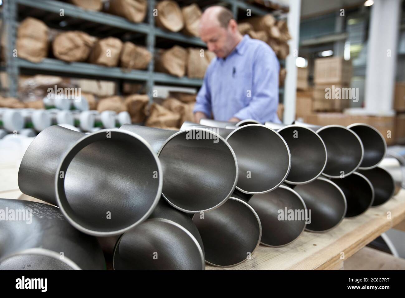 Uomini che lavorano in una fabbrica di acciaio, tubi corti in acciaio su ripiani. Foto Stock